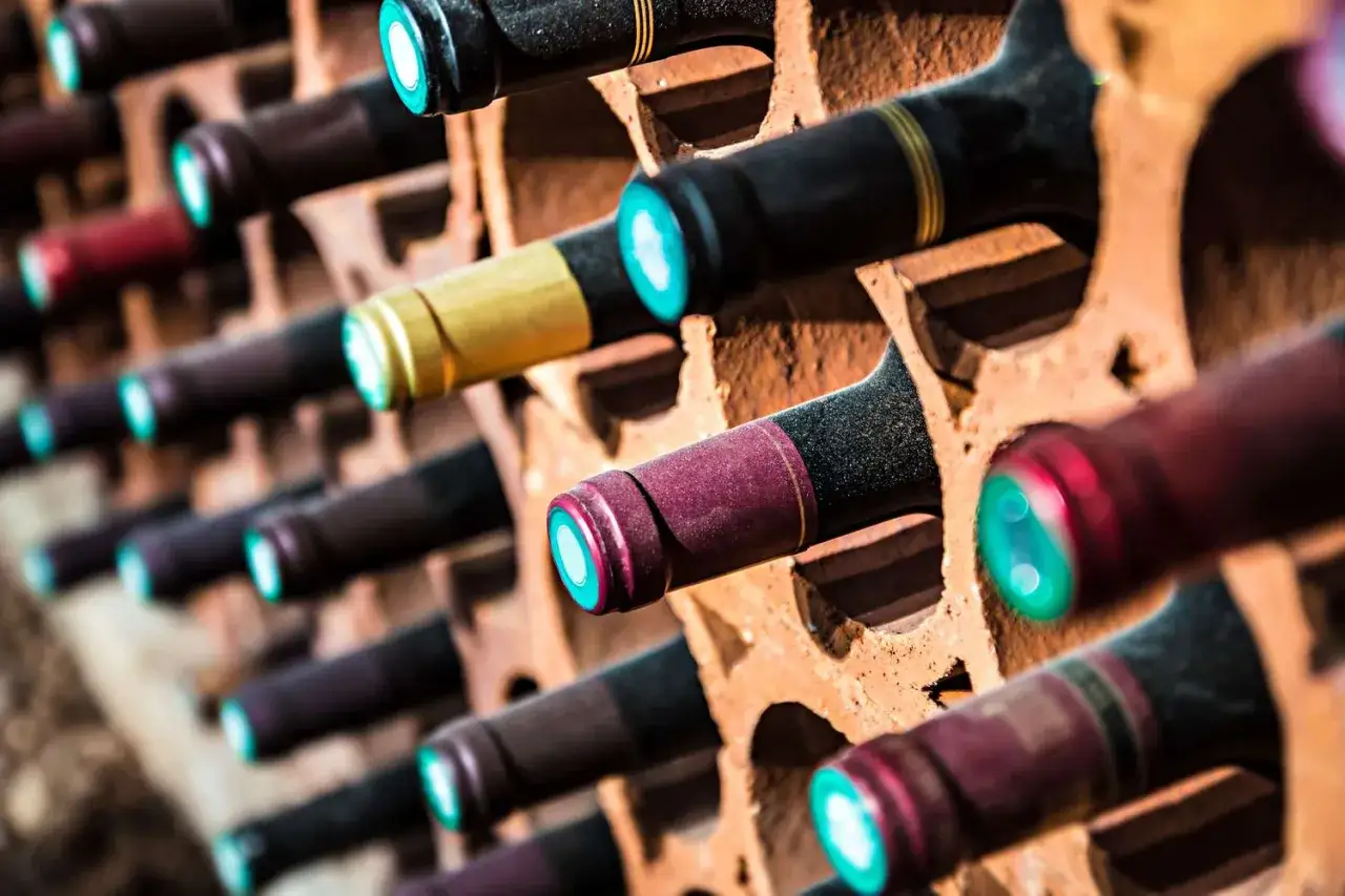 Des bouteilles de vin reposent dans une cave, évoquant la question : qu'est ce qu'un vin naturel ? Leurs bouchons colorés brillent.