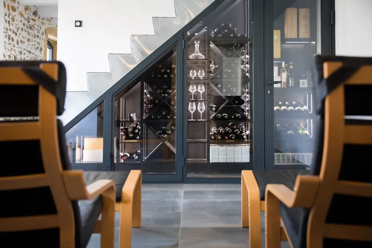 Une cave à vin moderne sous un escalier, avec des bouteilles et des verres à pied bien rangés.