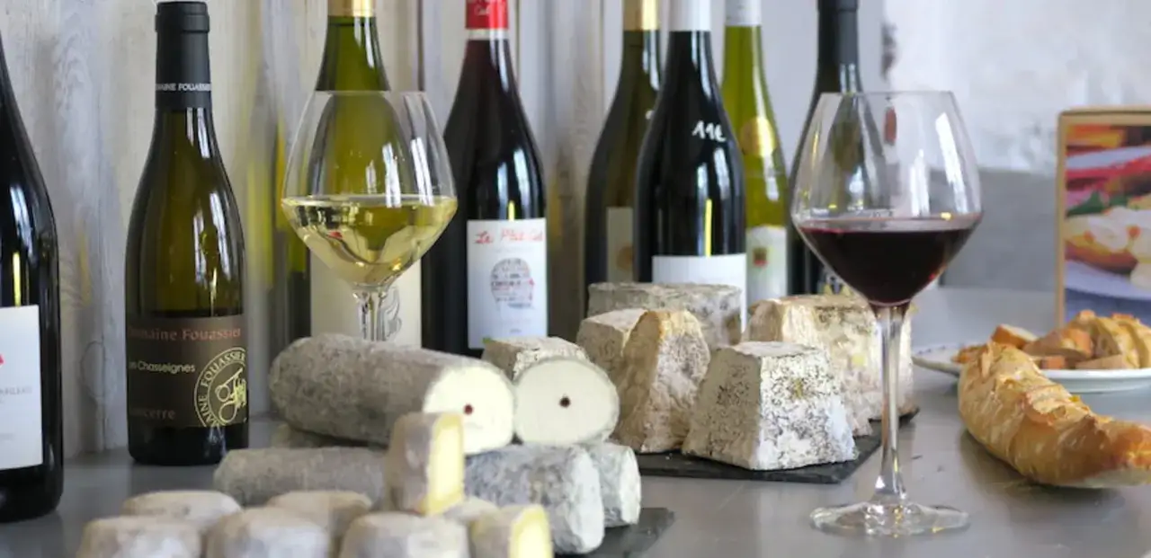D&eacute;gustation de vins et de fromage de ch&egrave;vre du Pays de la Loire, avec des bouteilles et des verres de vin, et une s&eacute;lection de fromages affin&eacute;s.