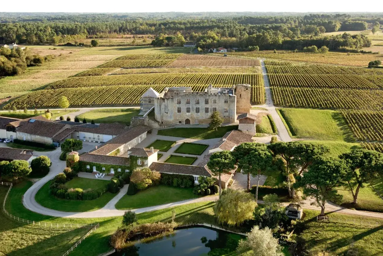 Ch&acirc;teau de Cazeneuve, propri&eacute;t&eacute; d'Alexandre de Lur Saluces, entour&eacute; de vignobles et de verdure, sous un ciel clair.