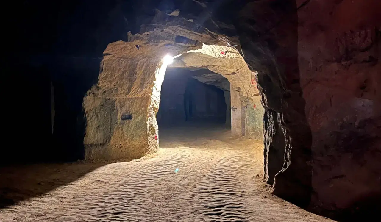 Un chemin s'enfonce dans une cave troglodyte éclairée par des lumières artificielles, révélant des parois rocheuses sculptées.