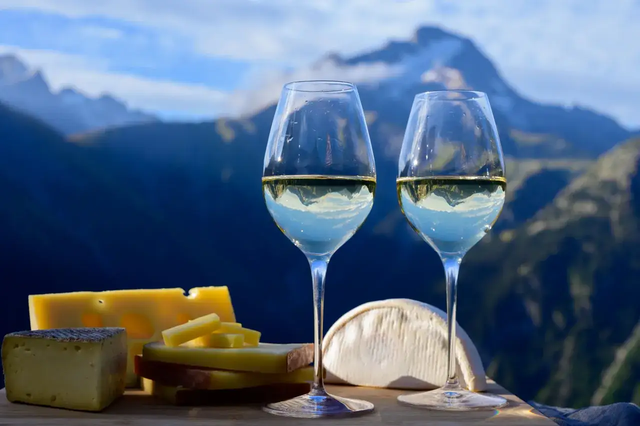 Deux verres de meilleur vin de Savoie blanc, accompagn&eacute;s de fromages savoyards, avec des montagnes majestueuses en arri&egrave;re-plan.