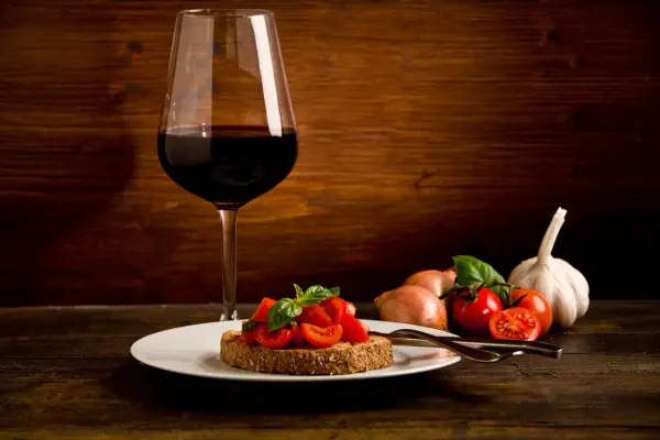 Bruschetta aux tomates fraîches et basilic, accompagnée d'un verre de vin rouge passe partout. Ail et oignons en arrière-plan.